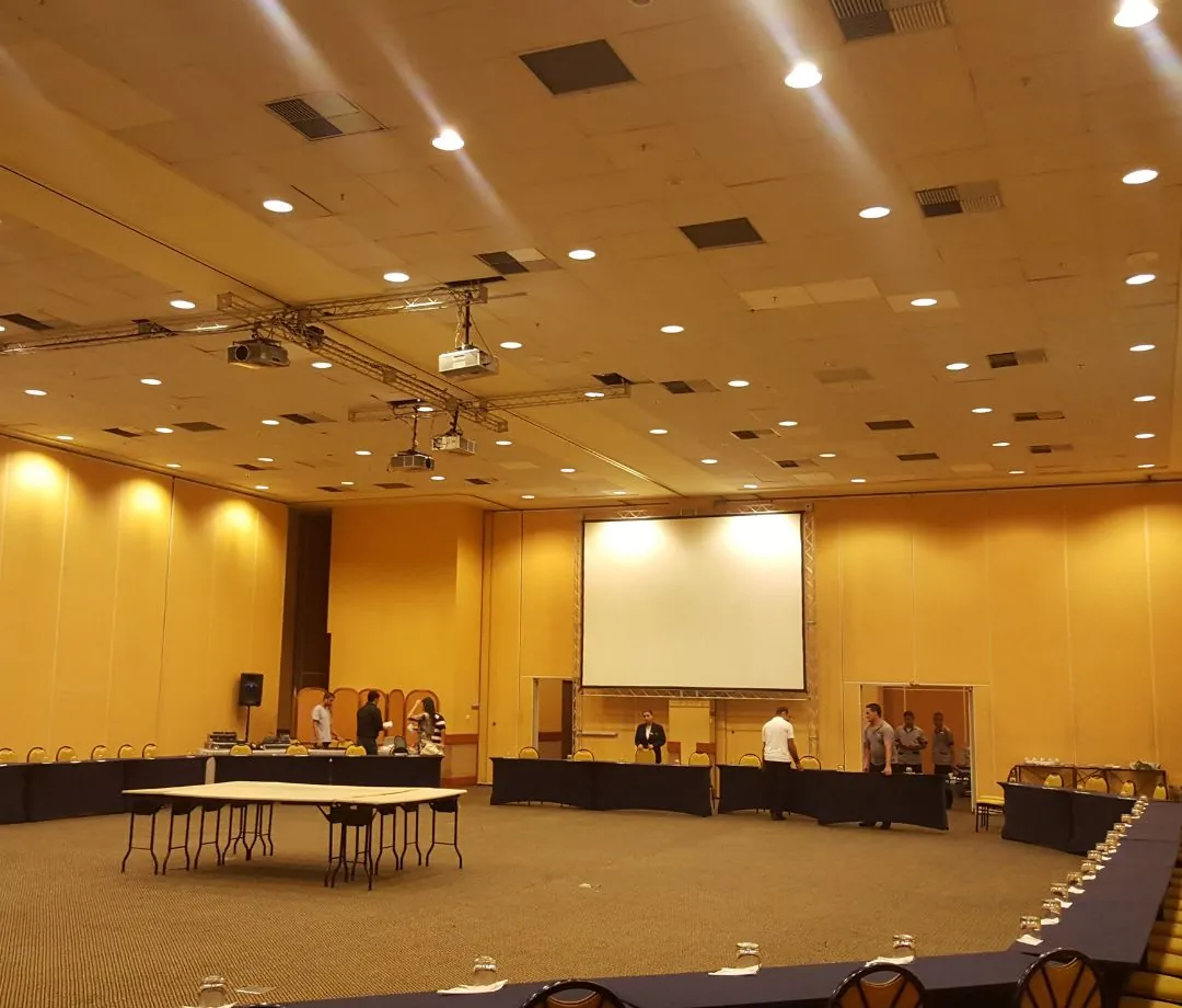 Salão de convenções com tela de projeção e mesas montadas