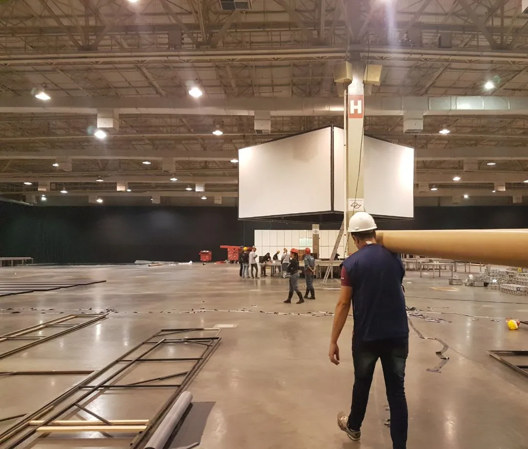 Técnico caminhando sob telão suspenso em pavilhão
